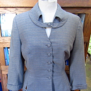 May include: A light blue blazer with a unique collar design and button-up front. The blazer has three-quarter sleeves and decorative buttons on the cuffs and sides. The jacket is displayed on a mannequin.