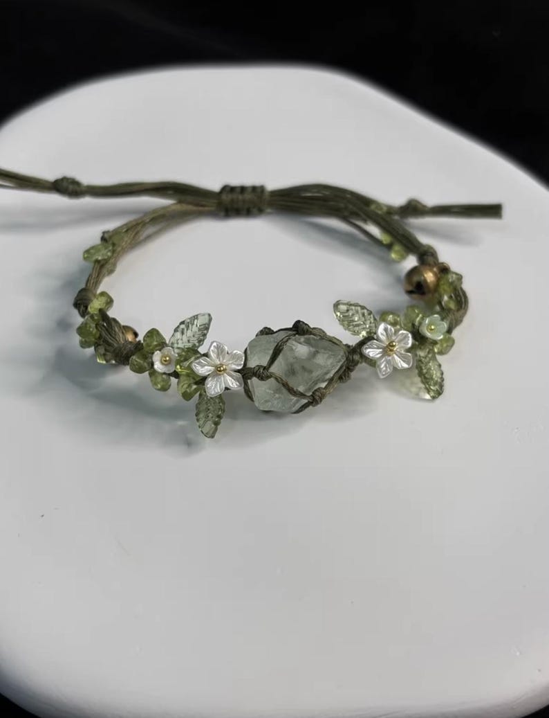 Pu&ograve; includere: Bracciale in macram&egrave; verde fatto a mano con un cristallo verde chiaro al centro. Il bracciale &egrave; decorato con piccoli fiori bianchi, foglie verdi e perline verdi. Questo bracciale regolabile &egrave; un gioiello unico.