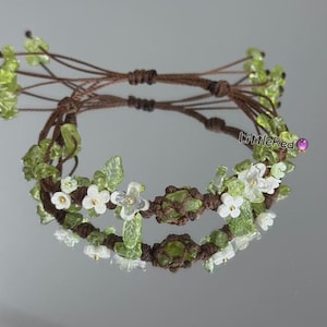 May include: A macrame bracelet with a brown cord, decorated with green gemstone beads and small white flower details. The bracelet is designed for everyday wear and is a unique piece of jewellery.
