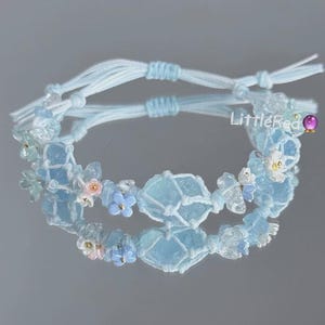 May include: Two light blue macrame bracelets with clear and blue beads and small flower accents. The bracelets are tied together with light blue string. The text "LittleRed" is visible on the right side.