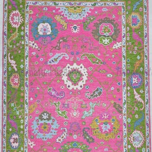 May include: A rectangular area rug featuring a vibrant hot pink central field adorned with intricate floral and paisley motifs in shades of blue, green, yellow, and white, framed by a wide, textured lime green border with colorful patterns.