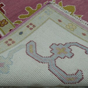 May include: Close-up of a section of a rug with a detailed pattern. The rug features a white background with a repeating floral design in shades of blue, red, and yellow. The border is a light green with a pink and yellow floral design.