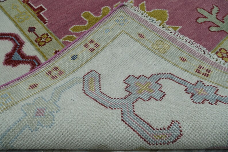 May include: Close-up of a section of a rug with a detailed pattern. The rug features a white background with a repeating floral design in shades of blue, red, and yellow. The border is a light green with a pink and yellow floral design.