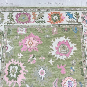 May include: A hand-knotted rug with a green field and a white border. The rug features floral patterns in pink, orange, and blue. The border has a repeating floral and geometric design. The rug is made of wool.