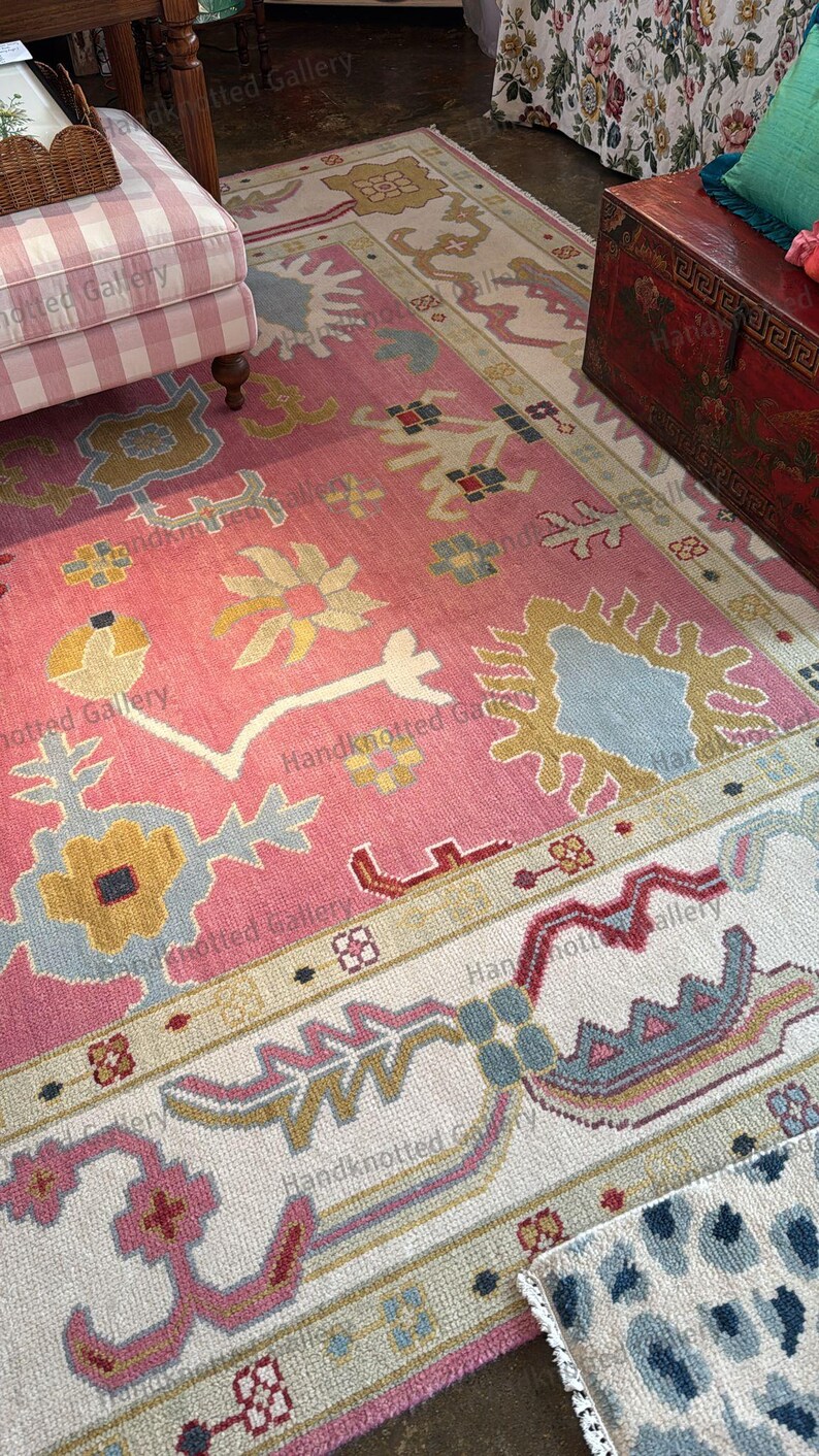 May include: A pink and ivory hand-knotted rug with a floral pattern. The rug features a central field of pink with stylized floral motifs in yellow, blue, and white. The border is ivory with complementary designs. The rug is a decorative floor covering.