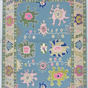 May include: A rectangular, hand-knotted rug with a light blue field and a beige border. The rug features floral and geometric patterns in pink, green, blue, and beige. The design includes stylized flowers and repeating border motifs, creating a traditional aesthetic.