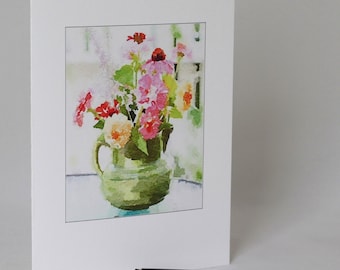 May include: A watercolor painting of a bouquet of pink, red, and yellow flowers in a green pitcher. The flowers are arranged in a vase on a table. The background is a soft, blurred watercolor wash.