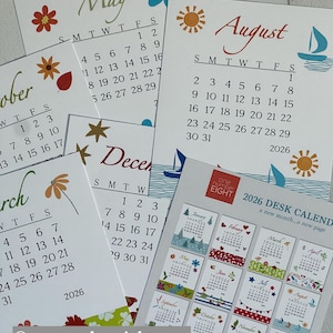 May include: A collection of 2026 desk calendars with floral and nautical illustrations. Each month is displayed on a separate card, featuring colorful designs and the year 2026. The calendars are from one number eight.