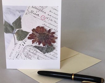May include: A white card with a pressed flower and leaves, a vintage stamp, and handwritten text that reads "Dauphin & Desor 25 Juillet 1891 en partance de 11 h", "Libby Wilkie: One Number Eight" is written at the bottom of the card.