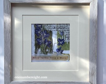 May include: A square wall art piece in a distressed white wood frame featuring pressed blue flowers, green textured paper, and handwritten script. A torn paper strip at the bottom displays the text Every Garden Tells a Story in brown ink.