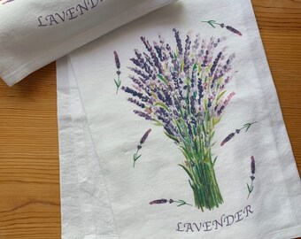 May include: White kitchen towel with a watercolor illustration of a bouquet of lavender flowers. The towel has the word "LAVENDER" printed in black at the top and bottom.