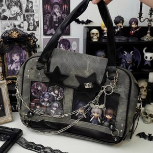 May include: A gray tote bag with black accents, star-shaped embellishments, and a chain detail. The bag features clear window pockets displaying anime-style character pins and figurines. The bag has a top handle and a shoulder strap.