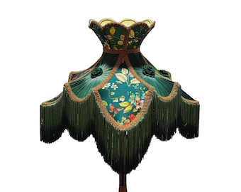 May include: A decorative lampshade with a dark green floral pattern and gold trim. The lampshade has a scalloped edge with long fringe and fabric roses. The floral design includes butterflies and colorful flowers.