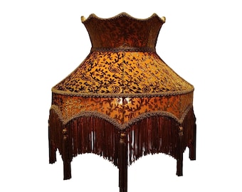 Könnte beinhalten: Eine dekorative Lampe mit einem großen, verzierten Lampenschirm. Der Schirm hat ein Paisley-Muster in Gold und Braun, verziert mit goldener Borte und dunkelbraunen Fransen. Die Lampe hat eine Vintage-Ästhetik.