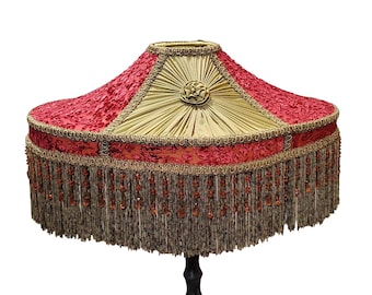 Puede incluir: Pantalla de lámpara decorativa con parte superior de terciopelo rojo y centro de satén dorado. La pantalla está adornada con trenza dorada y flecos de cuentas. Un artículo de decoración del hogar único.