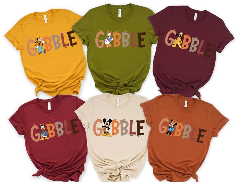 May include: A collection of six short-sleeved t-shirts in various colors, each featuring a different Disney character and the word "GOBBLE" in a playful font. The shirts are in shades of yellow, green, burgundy, tan, and orange.