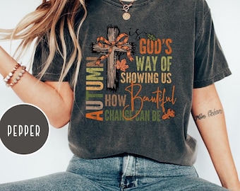 May include: Dark gray t-shirt with the text "Autumn is God's Way of Showing Us How Beautiful Change Can Be" and a cross design with a plaid bow. The shirt also has autumn leaves and the word "Pepper" on it.