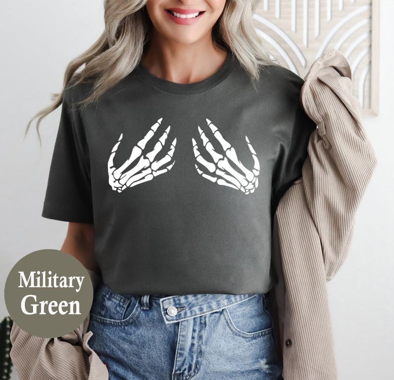May include: Military green t-shirt featuring a white skeleton hand graphic. The short-sleeved shirt is made of a soft material and is suitable for casual wear. The shirt is paired with blue jeans.