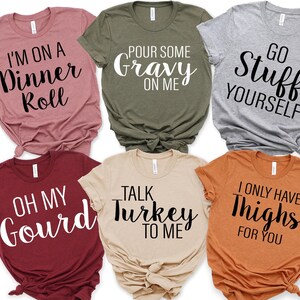 May include: Six short-sleeved t-shirts in different colours, each printed with a humorous Thanksgiving-themed phrase in black script. Phrases include "Pour Some Gravy on Me" and "Talk Turkey to Me."