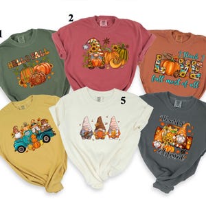 May include: A collection of six fall-themed t-shirts in various colors. Designs include pumpkins, gnomes, and the phrases "Hello Fall", "I think I love fall most of all", and "Thankful & Blessed".