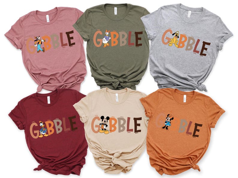May include: A collection of six t-shirts in various colors, each featuring the word "GOBBLE" in a playful font. Each shirt showcases a different Disney character, including Goofy, Donald Duck, Pluto, and Mickey and Minnie Mouse.