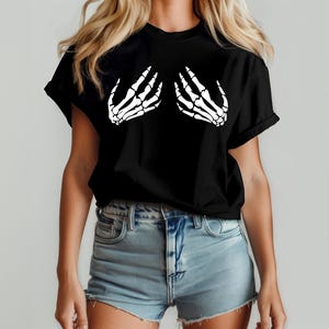 May include: Black t-shirt featuring a white skeleton hand graphic on the front. The graphic depicts two hands in a cupping gesture. The shirt is made of a soft material and has short sleeves.