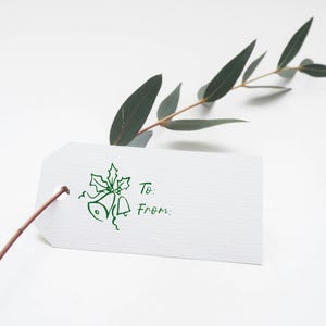 Pode incluir: Uma etiqueta de presente branca com um design verde de azevinho e sinos. A etiqueta tem as palavras "Para:" e "De:" impressas nela.