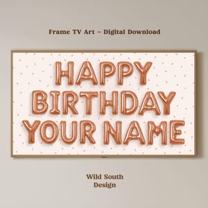 May include: A digital download for a Frame TV featuring the words "HAPPY BIRTHDAY YOUR NAME" in copper-colored balloon letters. The background is a light pink with small confetti-like shapes. The frame is a light brown color.