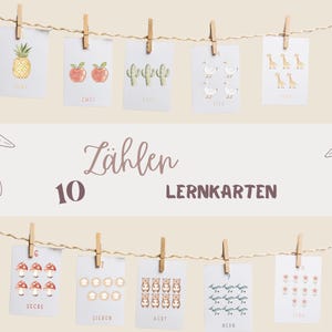May include: A set of ten educational flashcards, each featuring a different number and corresponding illustration. The cards are strung on a clothesline with wooden clothespins. The text "Zählen Lernkarten" and the number "10" are displayed on a banner.