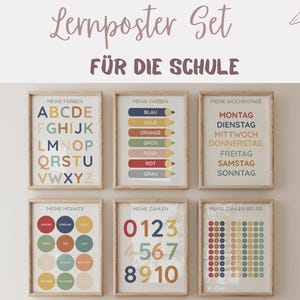 Könnte beinhalten: Ein Satz von sechs gerahmten Lernpostern mit Holzrahmen. Die Poster zeigen das Alphabet, Farben, Wochentage, Monate, Zahlen und Zahlen bis 100. Der Text ist auf Deutsch, mit einer sanften Farbpalette.