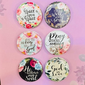 May include: A set of six 1.5-inch round custom magnets with floral designs and scripture quotes. The magnets feature phrases like "Grace upon Grace" and "God is Love" on a pink background.