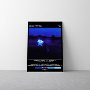 May include: A rectangular music album poster for Daniel Caesar's Never Enough. The design features a dark blue, grainy central image of a figure in white, surrounded by black borders with white text listing tracks, release date, and artist name.