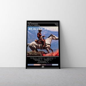 May include: A rectangular poster featuring a black border and white text. The central image shows a person in a brown shirt and hat riding a white horse against a mountain backdrop. The text reads The Strokes, Reality Awaits, and a tracklist.