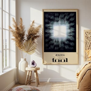 May include: A framed poster with the word "ÆNIMA" above "TOOL" in a black, stylized font. The artwork features a bright white square in the center, surrounded by a dark, textured background. The poster is displayed in a room with a window and decorative elements.