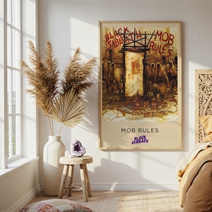 May include: A framed poster with the text "BLACK SABBATH / MOB RULES" in red and black. The artwork depicts a dark, stylized scene with figures and a central doorway. The poster is displayed in a well-lit room with a window and decorative elements.