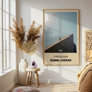 May include: A rectangular wall art print featuring the album cover for Freudian by Daniel Caesar. The print displays a person walking on a dark, angular structure against a light blue sky, with the text Freudian and Daniel Caesar below.
