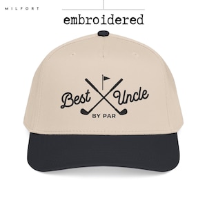 May include: A beige baseball cap with a dark navy blue brim and a dark navy blue button on top. The front features black embroidered text that reads Best Uncle BY PAR, accompanied by a graphic of two crossed golf clubs and a flag.