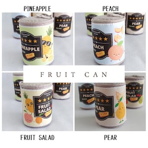 May include: A set of six felt fruit cans, each featuring a different fruit: pineapple, peach, pear, fruit salad, and two more pear cans. The cans are decorated with cartoon fruit characters and labels with the fruit name and "in syrup" or "in juice".