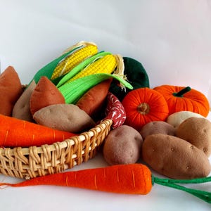 Puede incluir: Una colección de alimentos de fieltro, que incluyen zanahorias, batatas, maíz en la mazorca, calabazas y patatas, en una cesta de mimbre.