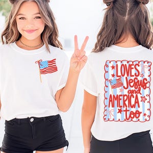 Puede incluir: Camiseta blanca con una bandera americana en la parte delantera y el texto "LOVES Jesus and AMERICA too" en la parte trasera. La camiseta se combina con pantalones cortos negros. El diseño presenta colores rojo, blanco y azul.