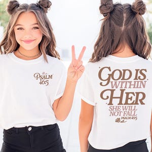 Puede incluir: Camiseta blanca con el texto "PSALM 46:5" en la parte delantera y "GOD IS WITHIN HER SHE WILL NOT FALL PSALM 46:5" en la parte trasera. La persona lleva pantalones cortos negros.