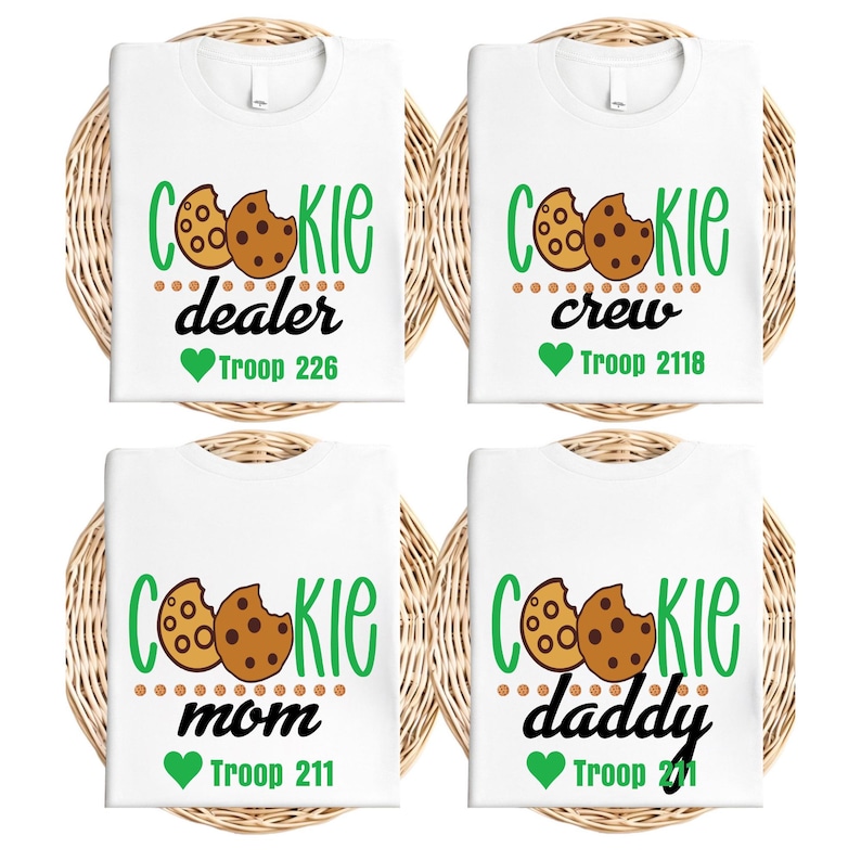 Peut inclure: Quatre t-shirts blancs avec des motifs sur le th&egrave;me des cookies. Chaque chemise pr&eacute;sente le mot "Cookie" en vert, un graphisme de cookie et un mot associ&eacute; comme "dealer" ou "crew". Chaque motif comprend un num&eacute;ro de troupe et un c&oelig;ur vert.