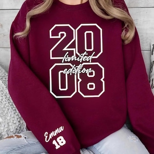 May include: A maroon sweatshirt with the numbers "20" and "08" in white, outlined font. The words "limited edition" are between the numbers. The name "Emma" and the number "18" are on the sleeve in white.