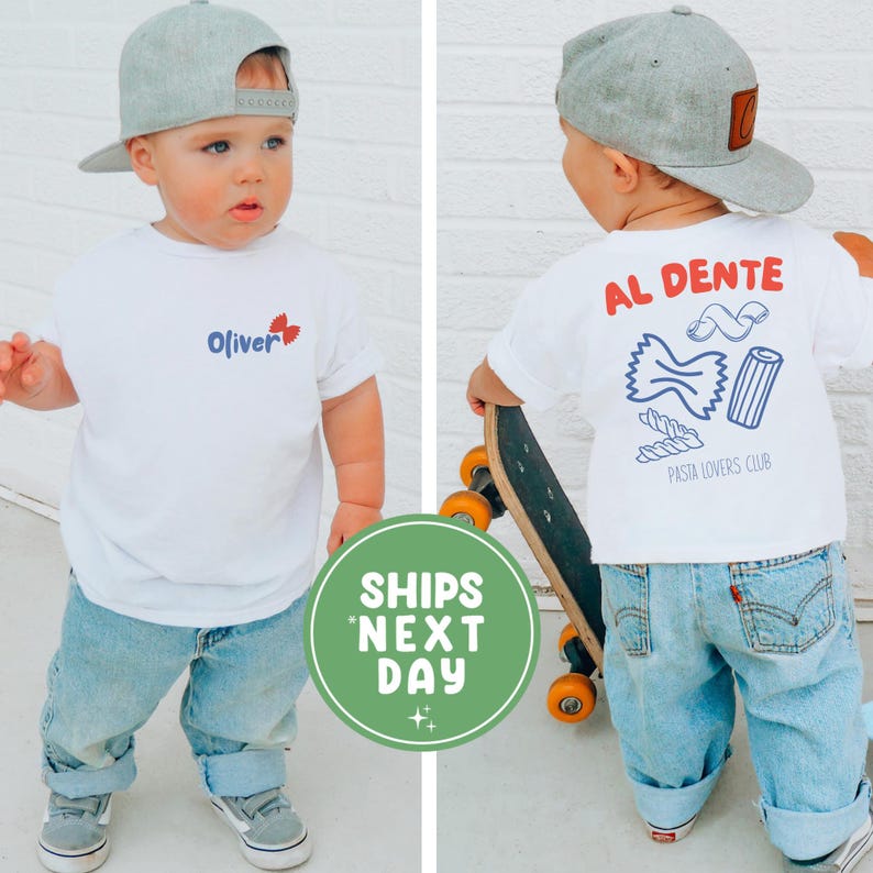 May include: A toddler wearing a white t-shirt and light blue jeans, paired with a gray baseball cap. The front of the shirt has the name "Oliver" and a red butterfly graphic. The back of the shirt says "AL DENTE" with pasta illustrations and "PASTA LOVERS CLUB."