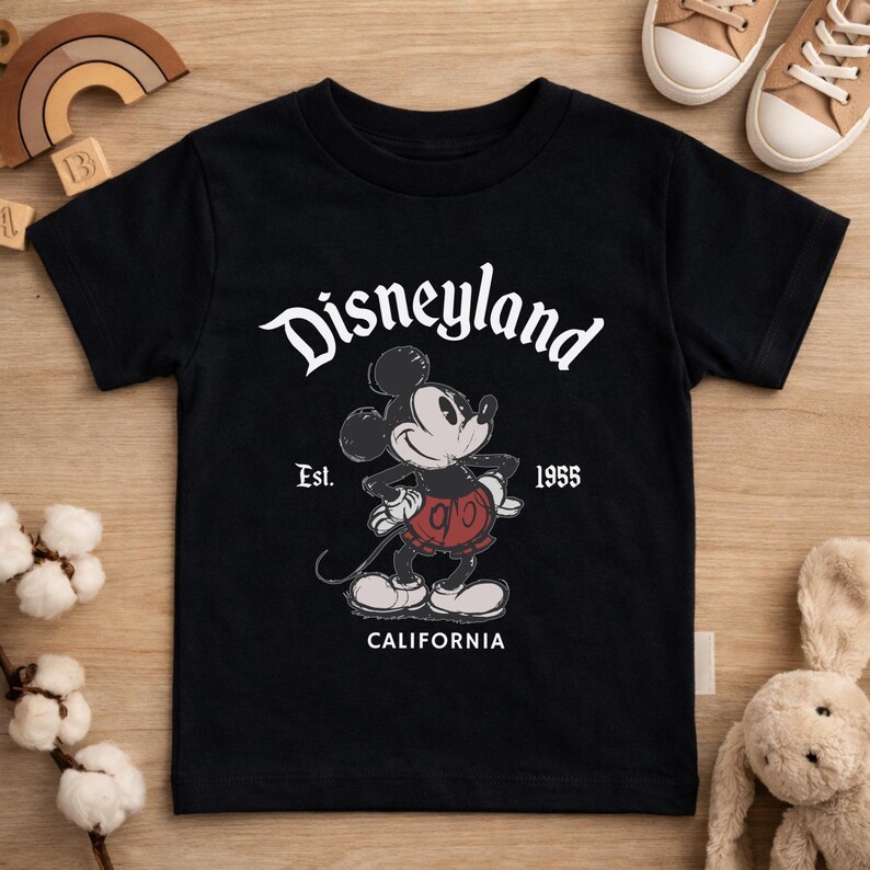 May include: Black t-shirt featuring a graphic of Mickey Mouse with the text "Disneyland" above and "Est. 1955 CALIFORNIA" below. The cartoon Mickey Mouse is in a standing pose, wearing red shorts and white gloves.