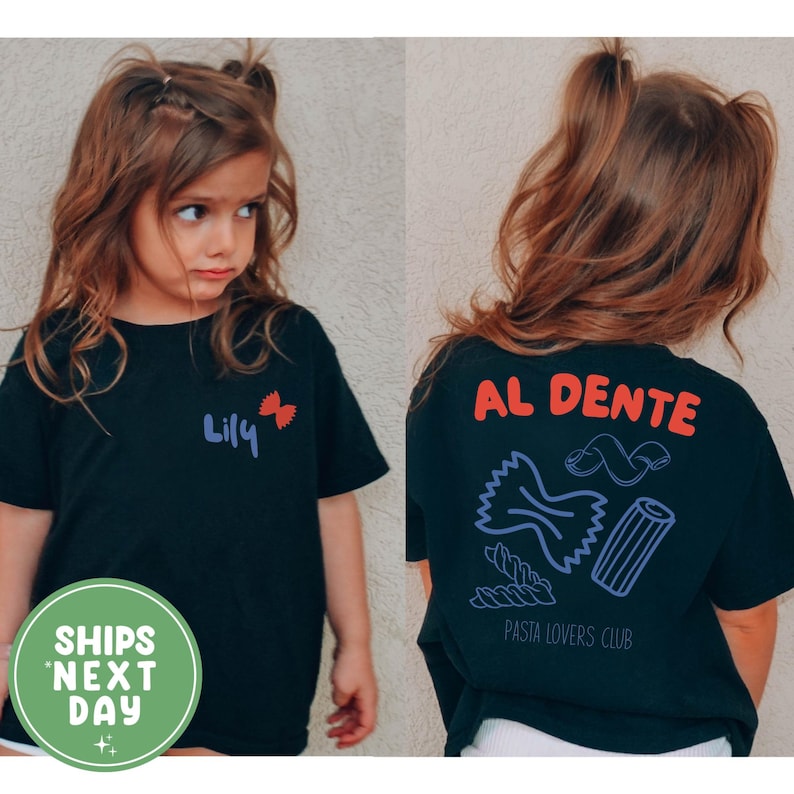 May include: Black t-shirt with the name "Lily" and a red bow graphic on the front. The back of the shirt features the words "AL DENTE" in red, pasta illustrations, and "PASTA LOVERS CLUB" in black. The shirt is for children.