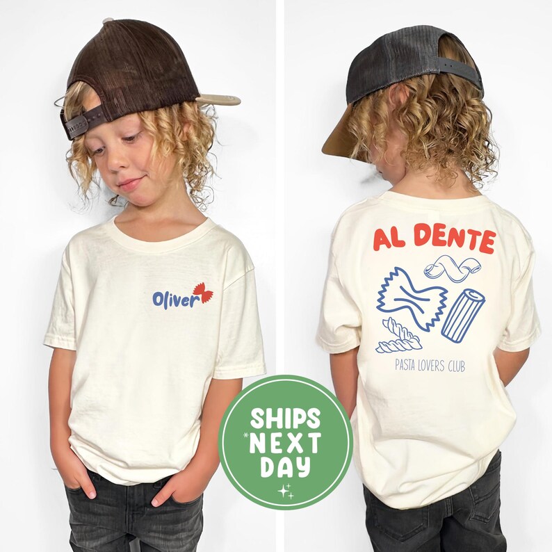 May include: A child wearing a cream-colored t-shirt and a brown baseball cap. The front of the shirt has the name "Oliver" in blue with a red leaf design. The back of the shirt features the words "AL DENTE" and pasta illustrations.
