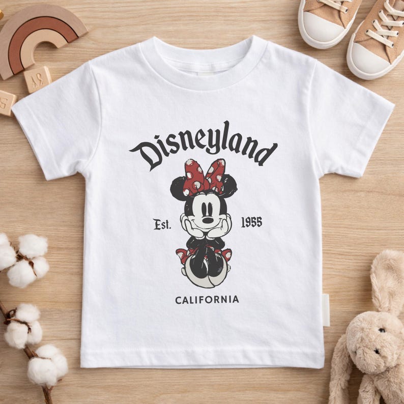 May include: White t-shirt featuring a Minnie Mouse graphic with a red polka dot bow and the text "Disneyland" above the character. The shirt also includes the text "Est. 1955" and "CALIFORNIA".