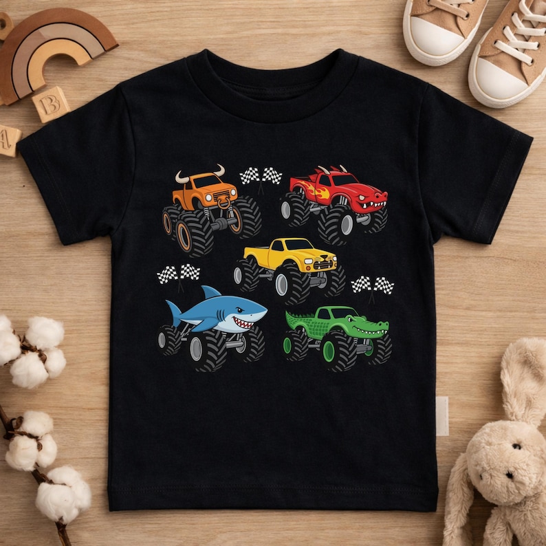 May include: Black t-shirt with illustrations of monster trucks in various colours. The trucks are orange, red, yellow, blue, and green, each with animal-themed designs. Checkered flags are positioned near each truck, implying a racing theme.
