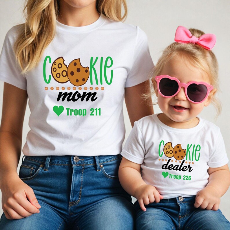 Peut inclure: Deux t-shirts blancs avec des motifs sur le th&egrave;me des cookies. L'un dit "Cookie Mom" avec un motif de cookie et "Troop 211". L'autre dit "Cookie Dealer" avec un motif de cookie et "Troop 226".